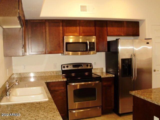 kitchen featuring light stone counters, visible vents, a sink, stainless steel appliances, and reddish brown cabinets