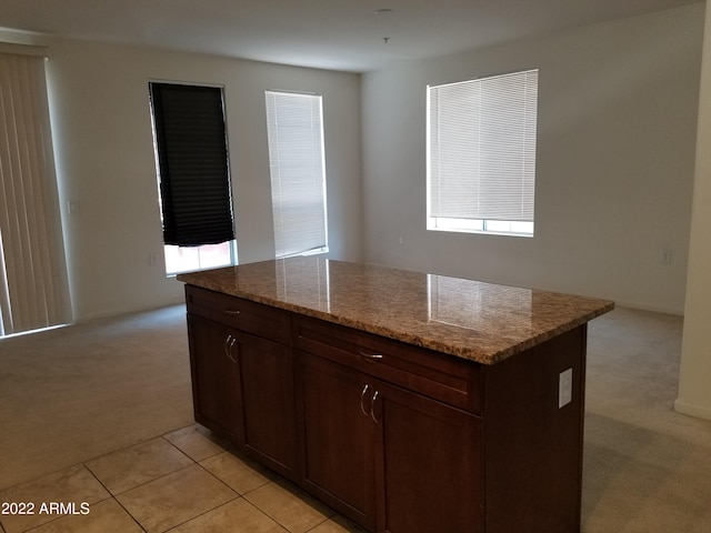 kitchen with light tile patterned flooring, light stone countertops, a kitchen island, and light carpet