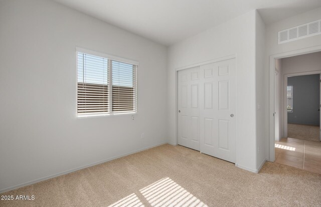 unfurnished bedroom featuring baseboards, a closet, visible vents, and light colored carpet