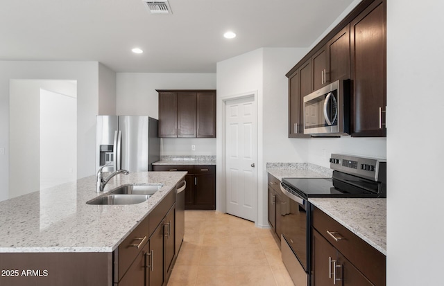 kitchen with visible vents, an island with sink, light stone counters, stainless steel appliances, and a sink