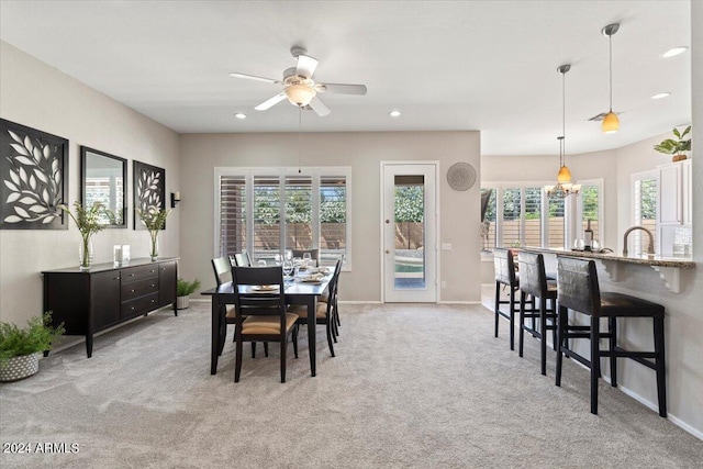 carpeted dining space with plenty of natural light, sink, and ceiling fan with notable chandelier