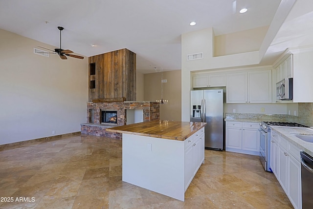 32710 N 71st St, Scottsdale, AZ 85266 - kitchen featuring appliances with stainless steel finishes, a stone fireplace, a ceiling fan, white cabinets, and a center island