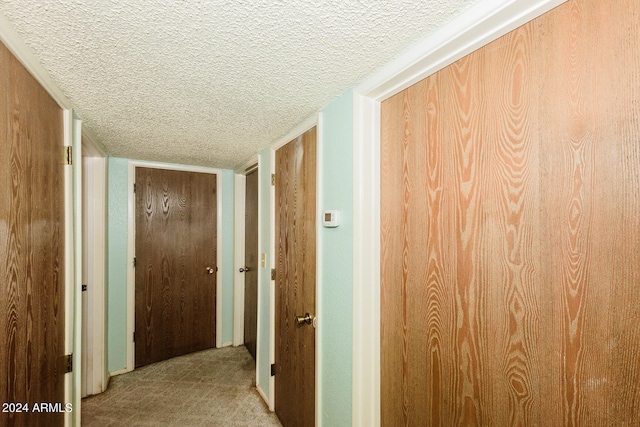 hall with light carpet, a textured ceiling, and wooden walls