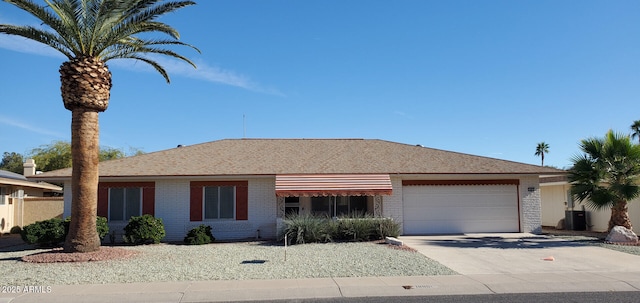 ranch-style house with a shingled roof, concrete driveway, an attached garage, central air condition unit, and brick siding