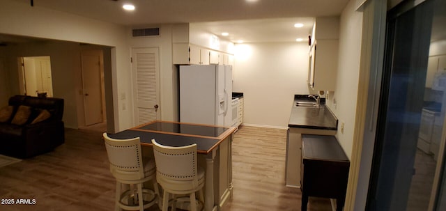 kitchen featuring sink, white refrigerator with ice dispenser, light hardwood / wood-style floors, white cabinetry, and a breakfast bar area