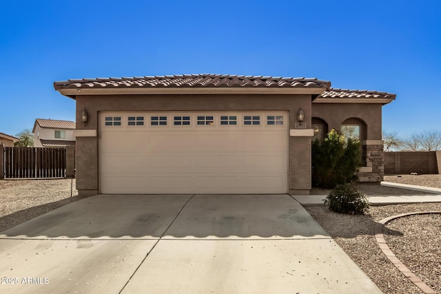 mediterranean / spanish-style home featuring a tile roof, stucco siding, concrete driveway, fence, and a garage