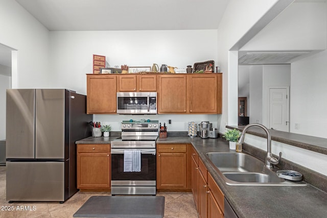 kitchen with light tile patterned floors, dark countertops, appliances with stainless steel finishes, brown cabinetry, and a sink