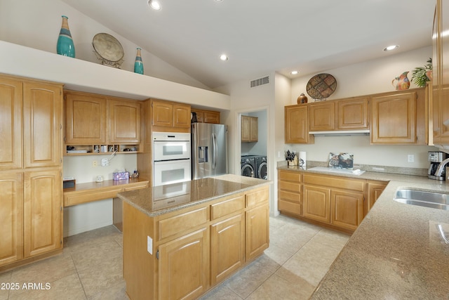 kitchen with sink, independent washer and dryer, stainless steel fridge with ice dispenser, light stone counters, and a kitchen island