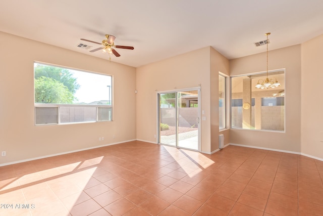 empty room featuring a wealth of natural light, tile patterned flooring, and ceiling fan with notable chandelier