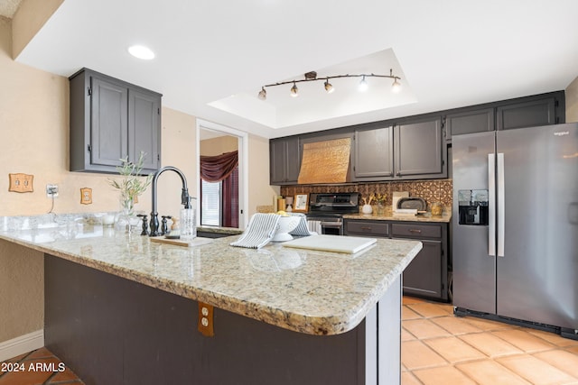 kitchen with a tray ceiling, kitchen peninsula, light stone counters, and appliances with stainless steel finishes