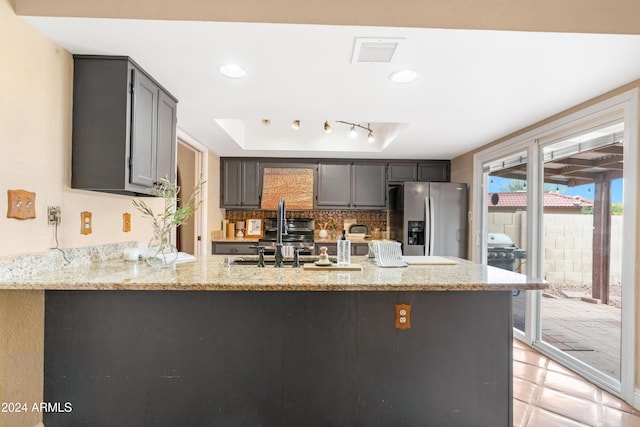 kitchen with a raised ceiling, kitchen peninsula, stainless steel fridge with ice dispenser, and sink