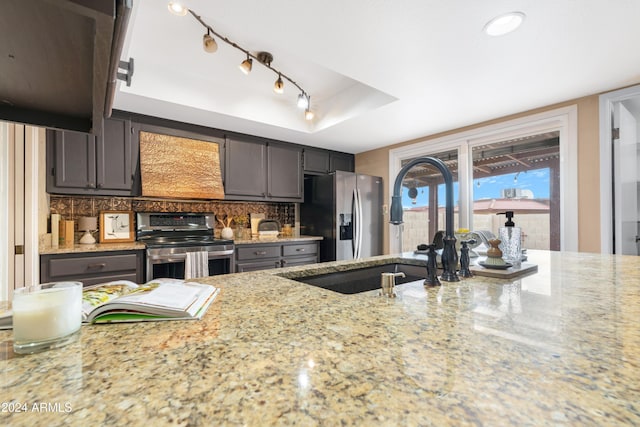 kitchen with decorative backsplash, light stone counters, stainless steel appliances, a raised ceiling, and sink