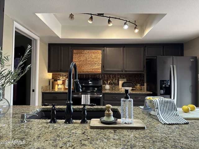 kitchen featuring dark brown cabinetry, light stone countertops, a raised ceiling, backsplash, and stainless steel fridge