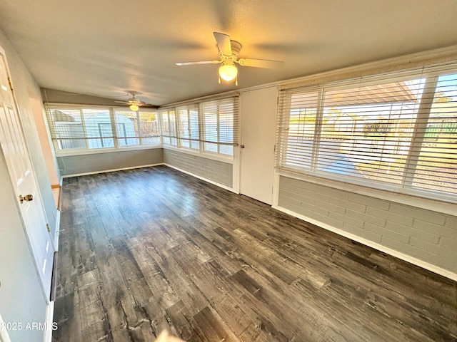 interior space with dark hardwood / wood-style floors, ceiling fan, and brick wall