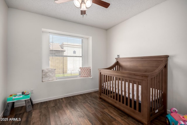 bedroom featuring a nursery area, a ceiling fan, wood finished floors, a textured ceiling, and baseboards