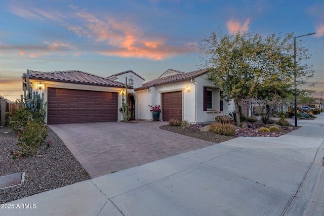 mediterranean / spanish-style home featuring an attached garage, stucco siding, decorative driveway, and a tiled roof