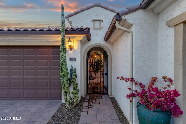 view of exterior entry with a garage, a tile roof, decorative driveway, and stucco siding