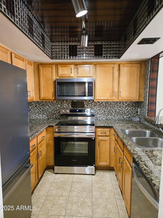 kitchen with decorative backsplash, dark stone countertops, appliances with stainless steel finishes, and a sink