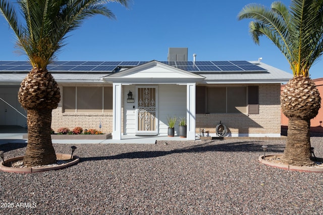 view of front facade with brick siding, covered porch, solar panels, and a shingled roof