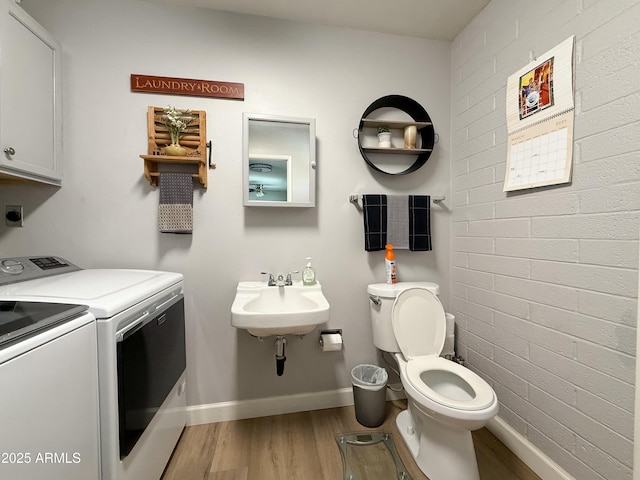 half bath with wood finished floors, baseboards, brick wall, separate washer and dryer, and a sink
