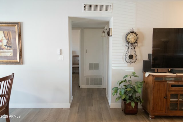 hall with visible vents, baseboards, and wood finished floors