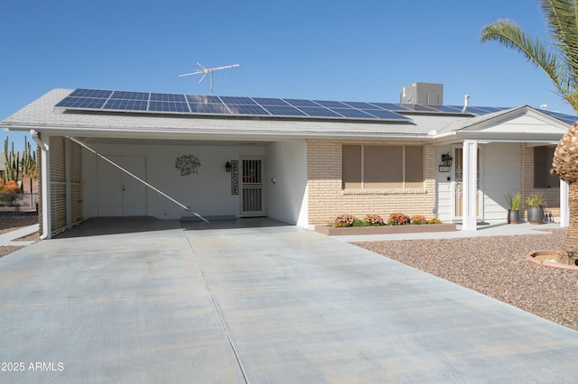 ranch-style home with an attached carport, solar panels, a shingled roof, concrete driveway, and brick siding