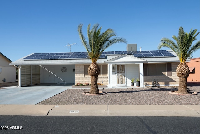 view of front of home featuring brick siding, roof mounted solar panels, concrete driveway, and a carport