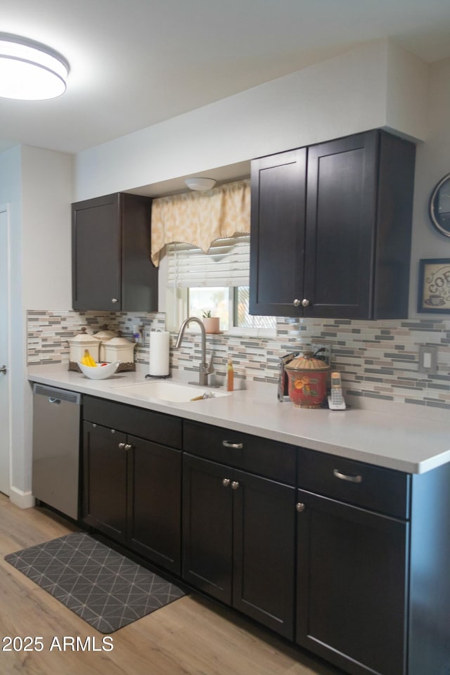 kitchen with light wood-style flooring, a sink, tasteful backsplash, stainless steel dishwasher, and light countertops