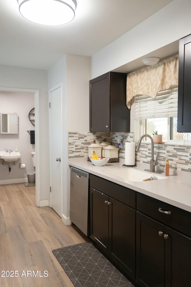 kitchen featuring light wood finished floors, tasteful backsplash, dishwasher, light countertops, and a sink