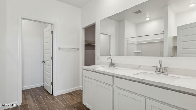 bathroom featuring wood finished floors, baseboards, a walk in closet, and a sink