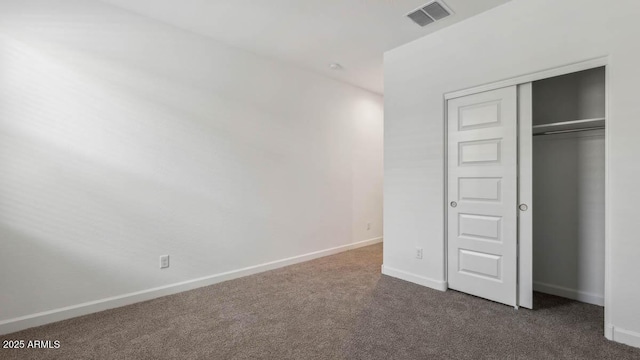 unfurnished bedroom with baseboards, visible vents, dark colored carpet, and a closet