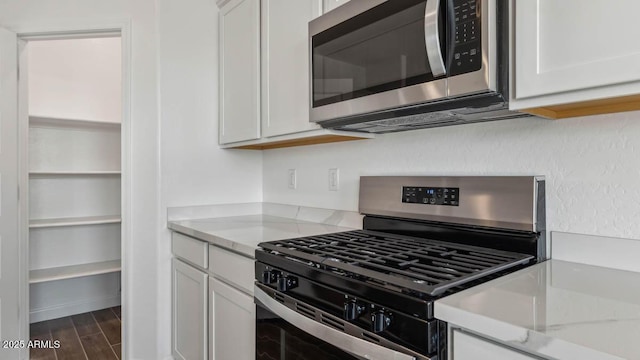 kitchen featuring white cabinetry, light stone countertops, dark wood-style flooring, and appliances with stainless steel finishes