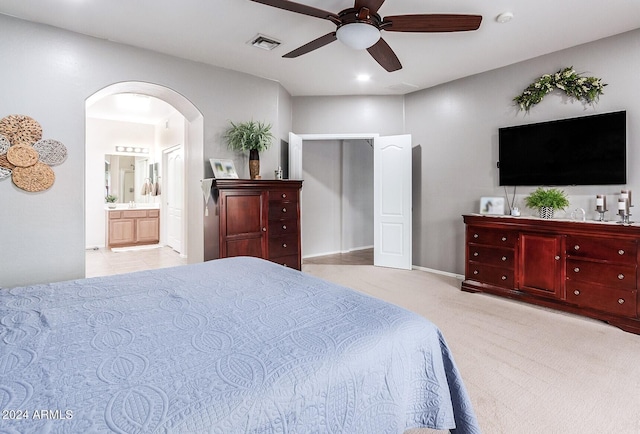 bedroom featuring light carpet, ensuite bathroom, and ceiling fan