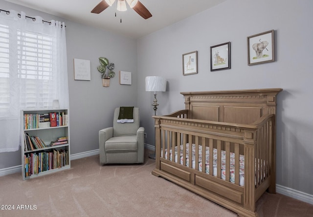 bedroom featuring a nursery area, light carpet, and ceiling fan