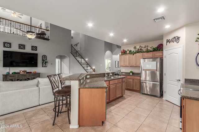 kitchen with stainless steel refrigerator, a kitchen island with sink, ceiling fan, a kitchen breakfast bar, and sink