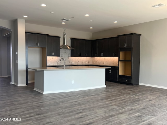 kitchen featuring hardwood / wood-style floors, a center island with sink, backsplash, sink, and wall chimney range hood