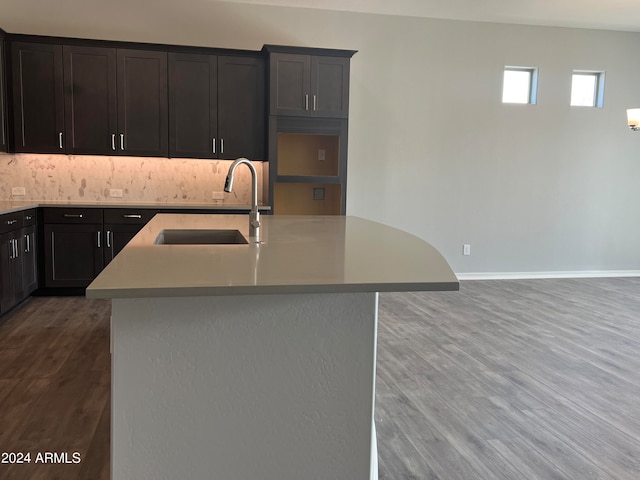 kitchen featuring sink, an island with sink, wood-type flooring, and backsplash