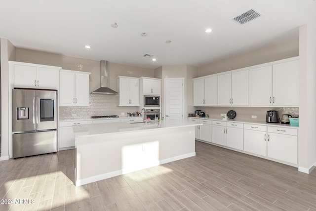 kitchen featuring a kitchen island with sink, white cabinets, wall chimney exhaust hood, light wood-type flooring, and appliances with stainless steel finishes