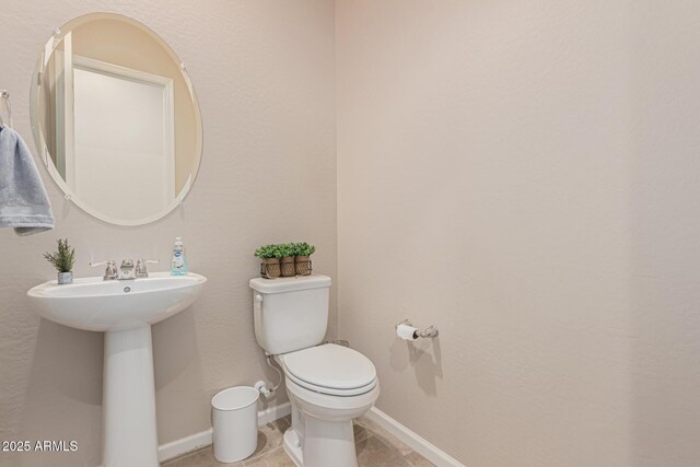 half bathroom featuring toilet, a sink, tile patterned flooring, and baseboards
