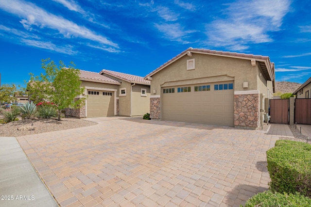single story home with stone siding, a garage, stucco siding, and a gate