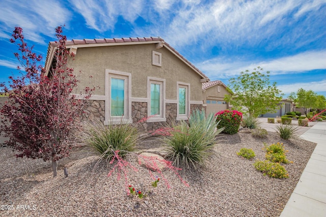 view of front of home featuring stucco siding, stone siding, a tiled roof, and a garage
