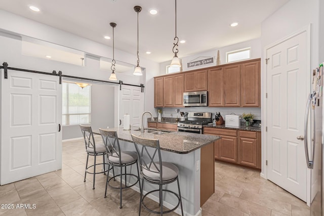 kitchen with appliances with stainless steel finishes, a barn door, a sink, a breakfast bar, and dark stone countertops