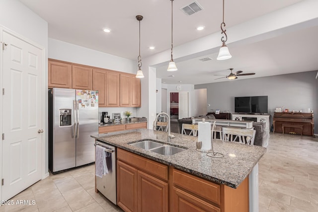 kitchen featuring appliances with stainless steel finishes, a sink, ceiling fan, an island with sink, and dark stone counters