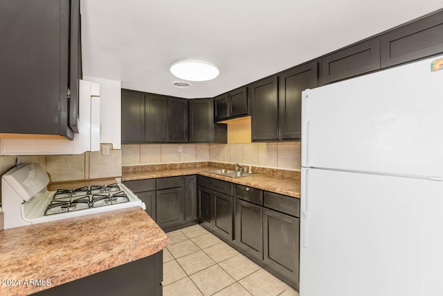 kitchen with white fridge, backsplash, range, light tile floors, and sink