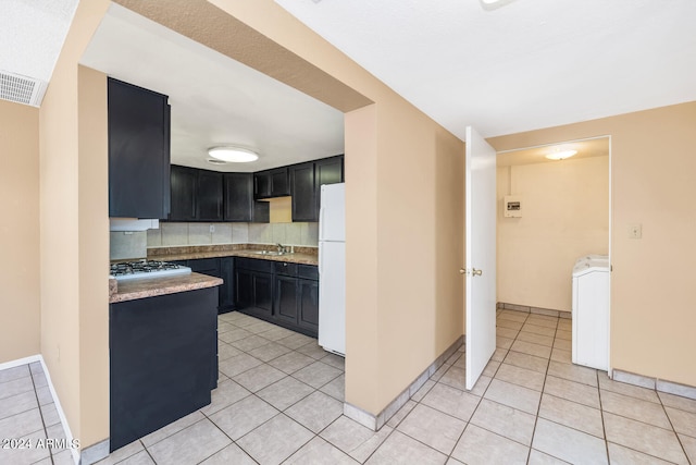 kitchen with backsplash, light tile floors, sink, washer / dryer, and white refrigerator