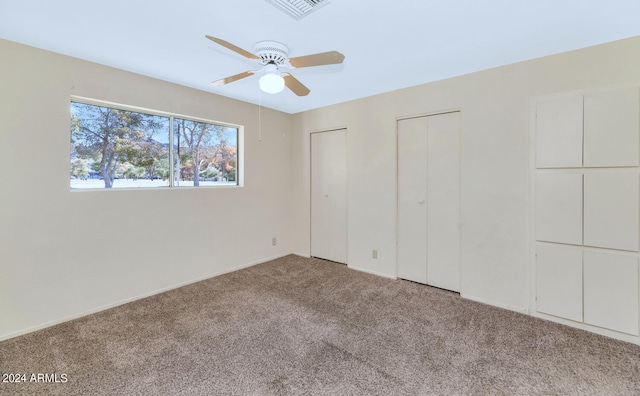 unfurnished bedroom with light carpet, multiple closets, and ceiling fan