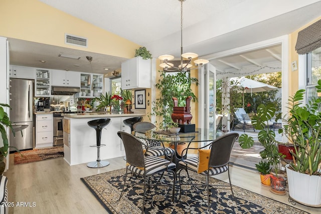 dining space featuring an inviting chandelier, lofted ceiling, light hardwood / wood-style flooring, and a textured ceiling