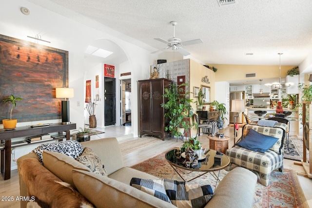 living room featuring ceiling fan with notable chandelier, vaulted ceiling, a textured ceiling, and light wood-type flooring