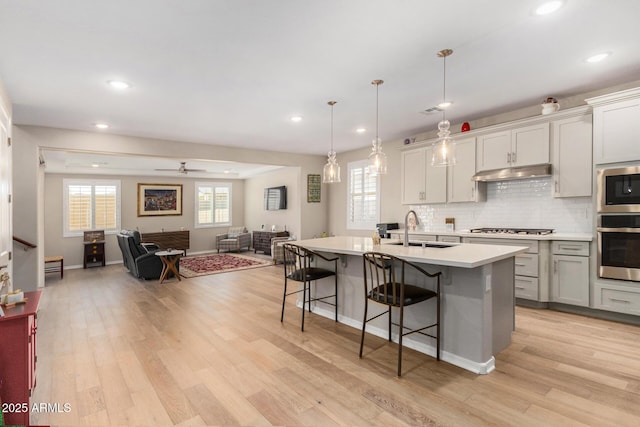 kitchen with an island with sink, ceiling fan, stainless steel appliances, pendant lighting, and sink