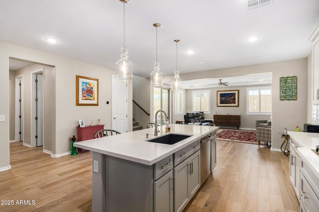 kitchen featuring decorative light fixtures, dishwasher, gray cabinets, sink, and a kitchen island with sink